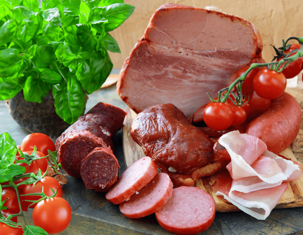 Rotes Fleisch und Wurstwaren auf einem Holzbrett als mögliche entzündungsfördernde Lebensmittel bei Rheuma.