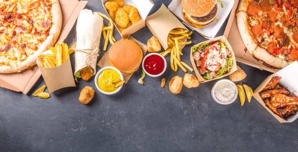 Tisch mit Burgern, Pommes und Pizza – Fastfood und stark verarbeitete Lebensmittel können Entzündungen fördern.