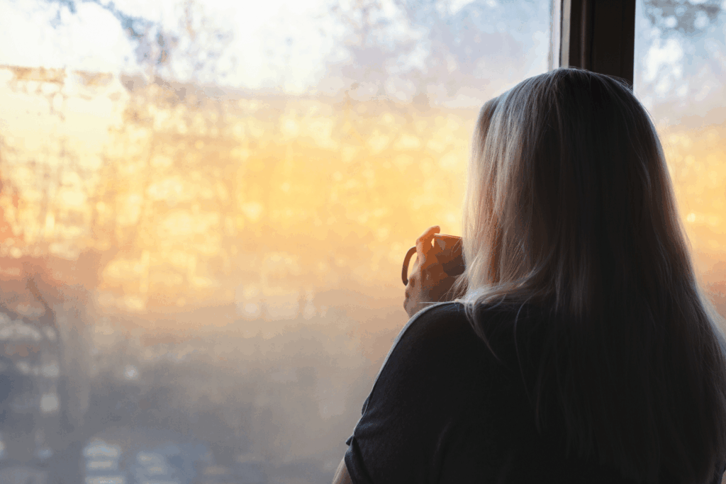 Frau blickt mit einer Tasse Tee in der Hand aus dem Fenster und wirkt nachdenklich – ein Sinnbild für die unsichtbare Belastung durch Rheuma und Fatigue.