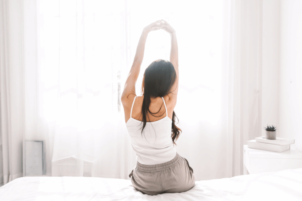 Frau sitzt morgens im Bett und streckt sich, um steife Gelenke bei Rheuma zu lockern.