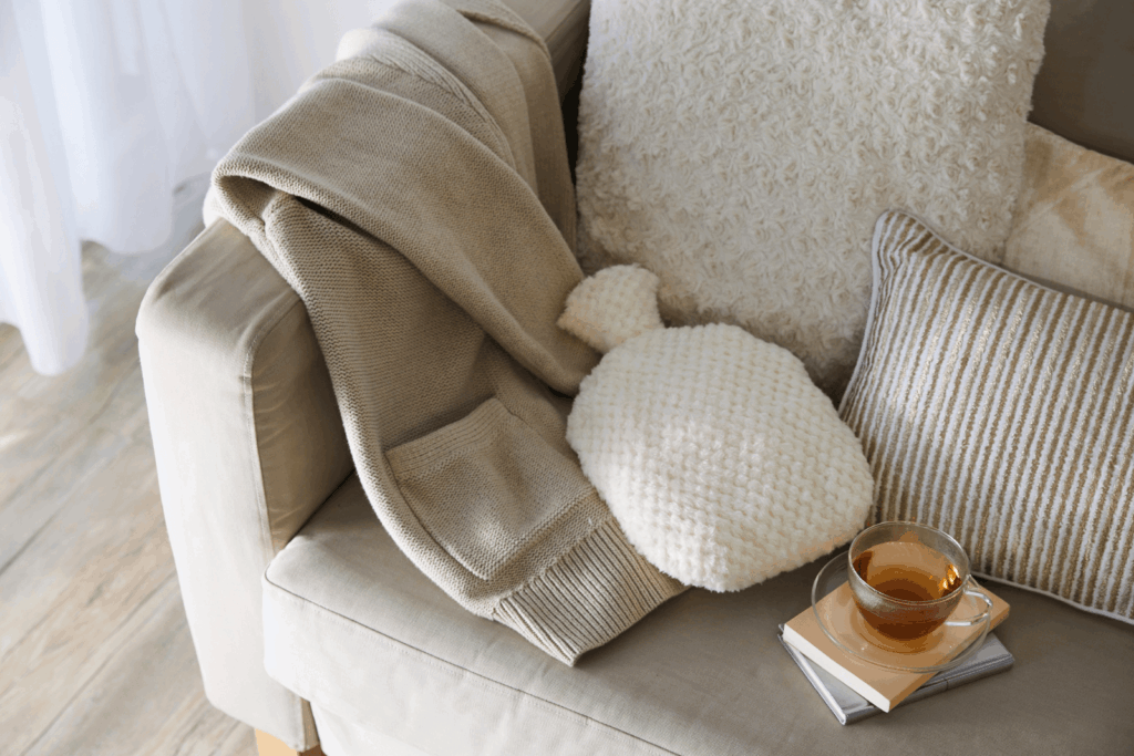 Gemütliches Sofa mit Decke, Wärmflasche und einer Tasse Tee als Symbol für Ruhe und Selbstfürsorge bei Rheuma und Fatigue.