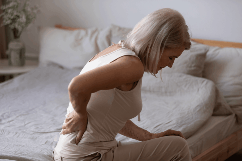 Frau mit Rückenschmerzen beim Aufstehen aus dem Bett – mögliches Symptom bei entzündlich-rheumatischen Erkrankungen